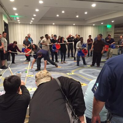Participants in an indoor setting engaging in a competitive team building activity with catapults, buckets, and various objects, demonstrating teamwork, strategy, and coordination during the Catapult to Success event. thumbnail