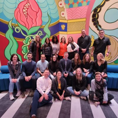 Team photo in front of a vibrant mural during a Mystery Bus team building event, capturing a moment of camaraderie and excitement. thumbnail