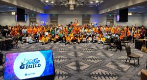 Large group photo at the Charity Guitar Build team building event, with participants holding guitars and celebrating teamwork and community impact.