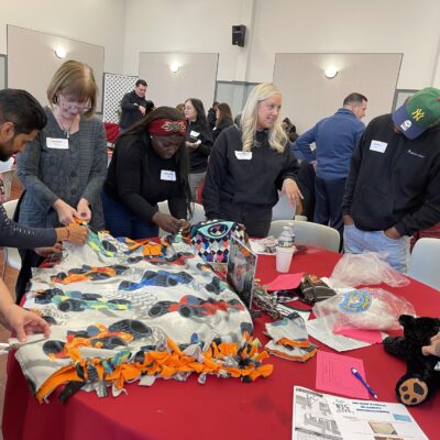 Team members actively collaborate to create cozy blankets during a Hope for the Holidays team building event, contributing to gift baskets that will bring warmth and joy to seniors this holiday season. thumbnail
