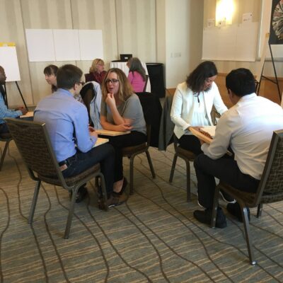 Small groups of participants engage in one-on-one discussions while holding wooden boards during a board-breaking team building activity focused on overcoming personal barriers. thumbnail