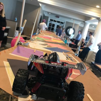 A remote-controlled car prepares to cross a large cardboard bridge designed by participants during the Bridging the Divide team building event. thumbnail