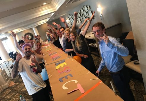 Participants proudly pose with their completed collaborative project during the Bridging the Divide team building event, celebrating creativity and teamwork in constructing a functional bridge model.