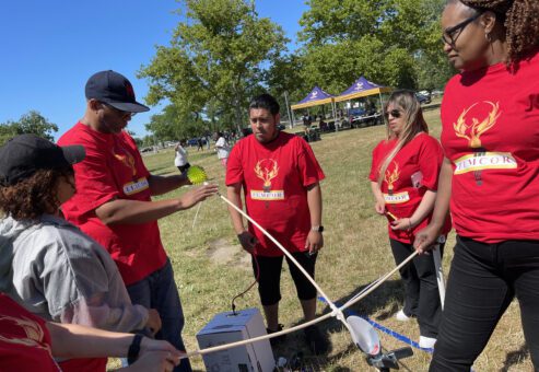 A team of participants in red shirts working together outdoors on constructing a catapult during the Catapult to Success team building activity, showcasing collaboration, creativity, and strategic planning.