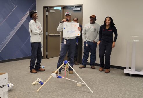 A team presenting their catapult design called 'The Rocket Launcher' during an indoor segment of the Catapult to Success team building activity, showcasing creativity, teamwork, and presentation skills.