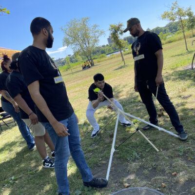 Participants outdoors collaborating on building a catapult during the Catapult to Success team building activity, showcasing teamwork, problem-solving, and creativity in a natural setting. thumbnail