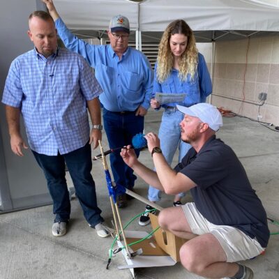 A group of four participants outdoors working together to assemble a small catapult during the Catapult to Success team building activity, emphasizing teamwork, innovation, and hands-on problem-solving. thumbnail