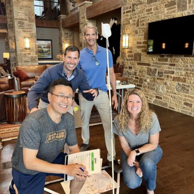 A group of four participants smiling and posing indoors with a constructed catapult during the Catapult to Success team building activity, emphasizing teamwork, innovation, and collaborative problem-solving. thumbnail