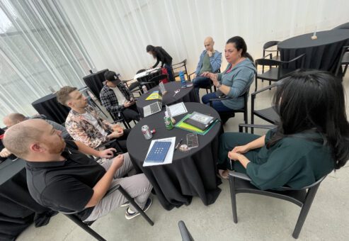 Group of team members sitting around a round table engaged in discussion on how to make a movie and what story to tell during the Corporate Film Festival team building.