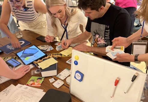 Team members actively engaged in solving a mystery during the 'Corporate CSI' team building event. Participants are examining evidence cards, taking notes, and using digital tools on tablets to analyze clues.