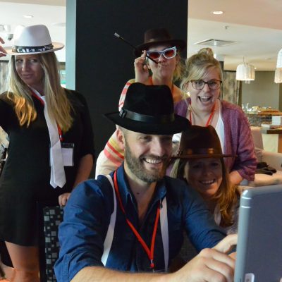 A team dressed in fun hats and posing for a photo during the Escape the Mob team building event, combining creativity and teamwork to solve the mystery. thumbnail