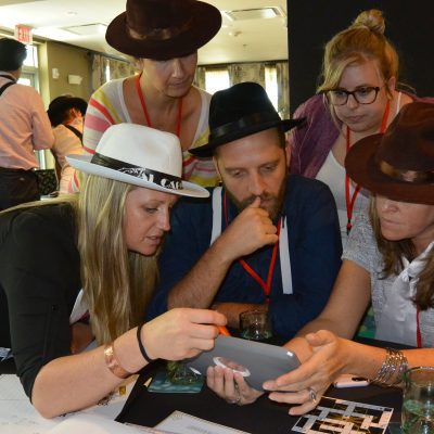 A focused team in the Escape the Mob team building challenge works together using an iPad to solve clues and establish their alibi in this high-energy mystery event. thumbnail