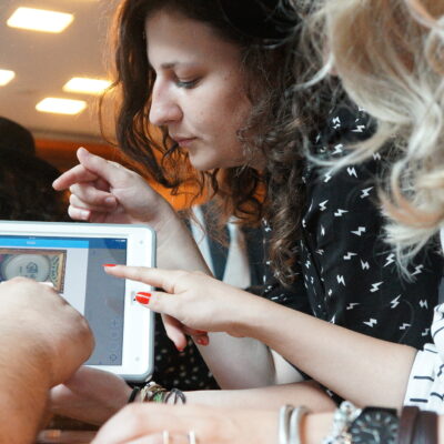 Three people closely examining a clue on a tablet screen during the 'Escape the Mob' team building activity. They are focused and engaged in solving a mystery, collaborating to piece together information and create a strategy for the game. thumbnail