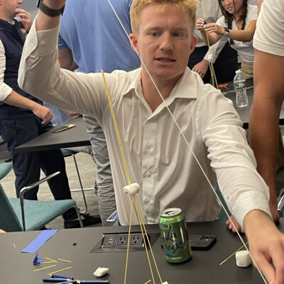A participant at a corporate team building event working on a hands-on challenge, constructing a tower using spaghetti and marshmallows. The activity encourages problem-solving, creativity, and teamwork. thumbnail