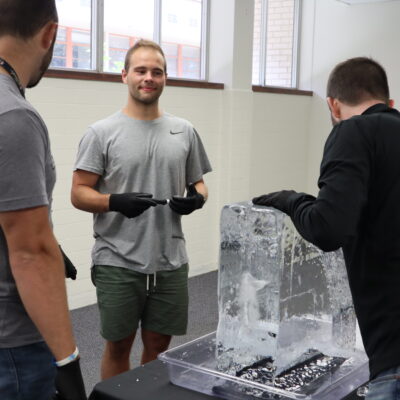 A group of participants works together, chiseling an ice block during a Team building Ice Sculpting event, showcasing teamwork and creativity. thumbnail