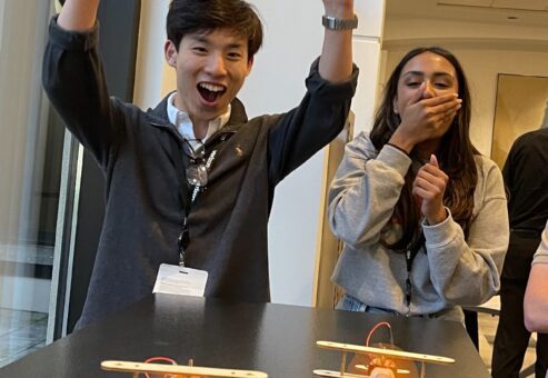 Two participants celebrating and smiling after successfully assembling and testing their miniature airplanes during the STEM Speedway team building activity, showcasing excitement, teamwork, and hands-on learning with STEM kits.