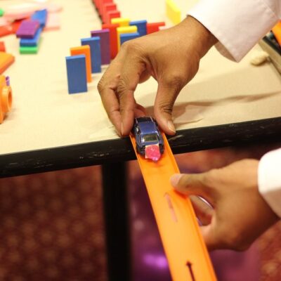 Close-up of a participant placing a toy car on a track as part of a hands-on activity during the Domino Effect team building event. thumbnail