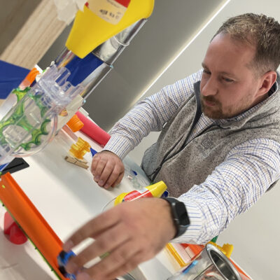 Participant working on a hands-on project during the Domino Effect team building event, focusing on creating Rube Goldberg-inspired contraptions to encourage creativity, problem-solving, and collaboration. thumbnail