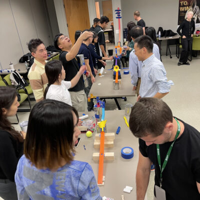 Participants working together to build a complex contraption during the Domino Effect team building activity. thumbnail