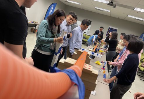 Teams working together to build an intricate Rube Goldberg machine during the Domino Effect team building activity.