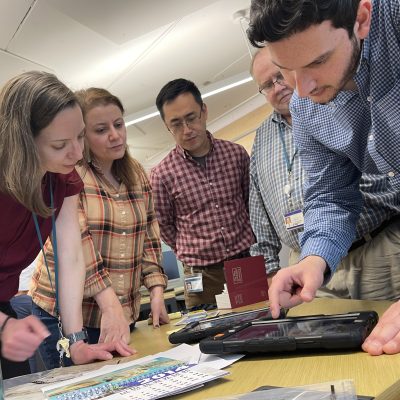 Team members collaboratively examining a virtual crime scene on a tablet during the Corporate CSI team building activity. thumbnail