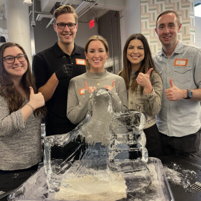 A team proudly poses with their completed ice sculpture during a Team building Ice Sculpting event, showcasing their creativity and teamwork in crafting the intricate design. thumbnail