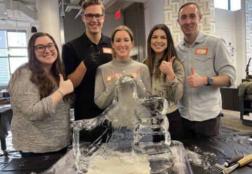 A team proudly poses with their completed ice sculpture during a Team building Ice Sculpting event, showcasing their creativity and teamwork in crafting the intricate design.