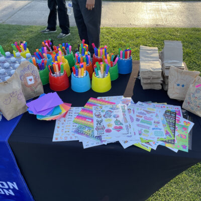 Table set up with colorful markers, stickers, and brown paper bags ready to be decorated during a corporate charitable team building event. thumbnail