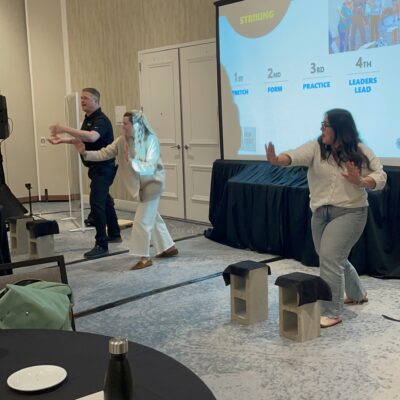 Two participants practice board-breaking techniques on stage during a team building event, guided by a facilitator. thumbnail
