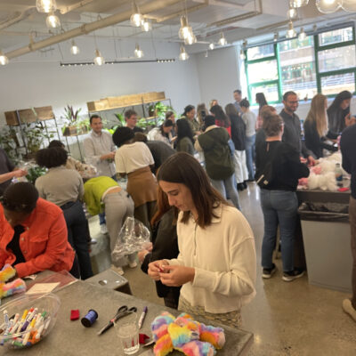 A large group of people working together to assemble donation kits during a busy corporate charitable team building event called The Donation Station. thumbnail