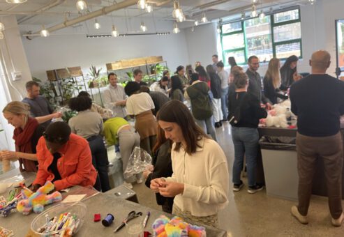 A large group of people working together to assemble donation kits during a busy corporate charitable team building event called The Donation Station.