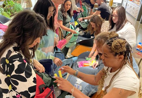 Participants in the 'Tools for Schools' event working together to fill backpacks with essential school supplies such as highlighters, notebooks, and pencils.