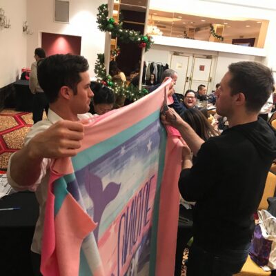 Two team members work together to prepare a fleece blanket during a holiday-themed team building event, contributing to gifts for seniors as part of the Hope for the Holidays program. thumbnail