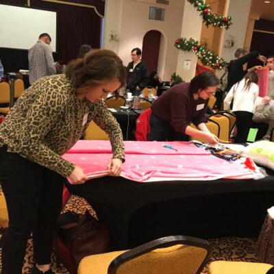 Participants at the Hope for the Holidays team building event work together to craft personalized blankets, spreading warmth and cheer to local seniors during the festive season. thumbnail