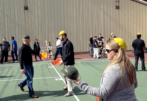 Teams participating in the Catapult to Success team building activity, engaging in hands-on construction of catapults while strategizing and collaborating on a tennis court setting.