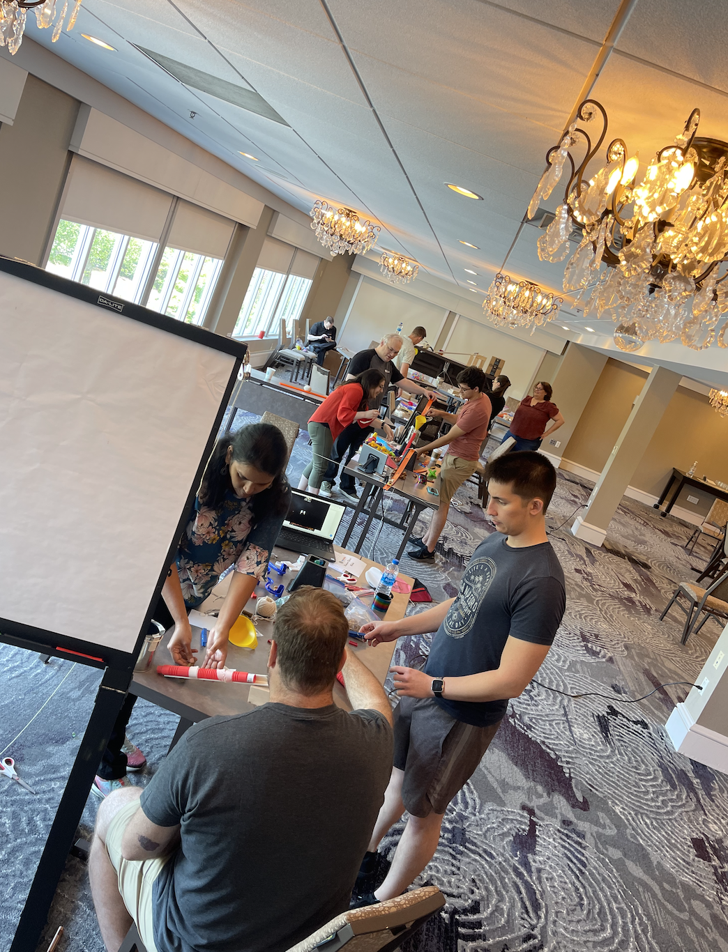 Teams working together in a spacious room, building creative contraptions during the Domino Effect team building event. thumbnail