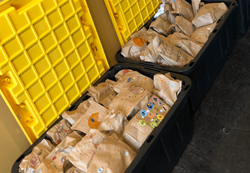 Large containers filled with decorated brown paper bags, ready for donation at a corporate charitable team building event.