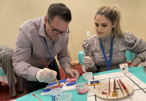 Two participants collaborate on painting a section of a mural during The Big Picture team building event, focusing on precision and teamwork to contribute to the larger artwork.